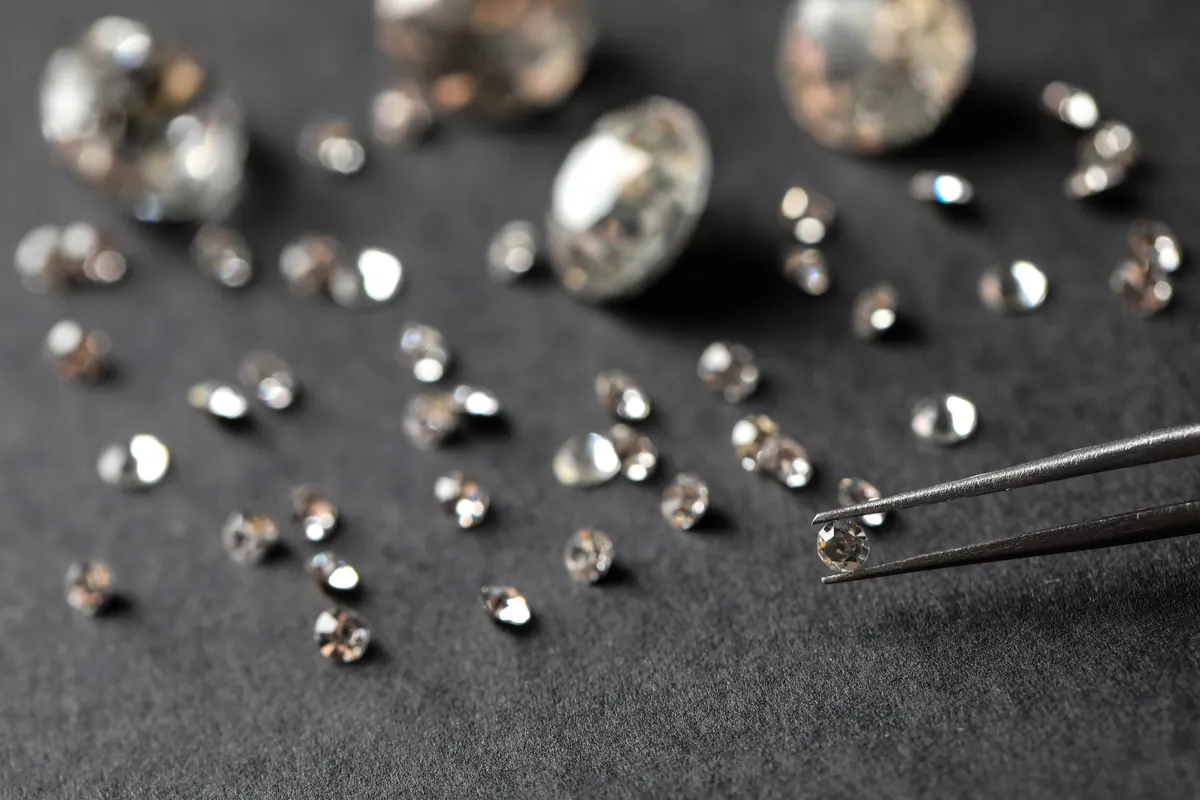 Metal tweezers holding a brilliant cut diamond above loose stones