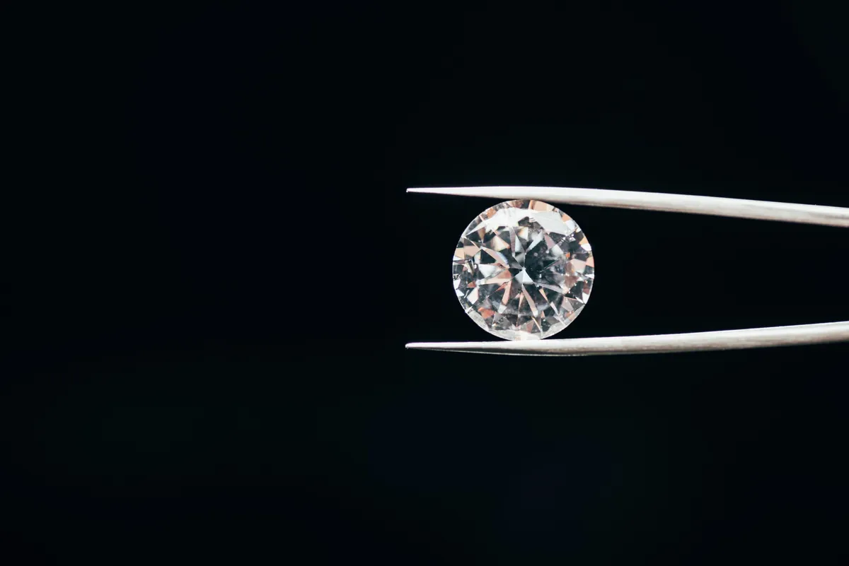 A round brilliant diamond held by tweezers against a black background