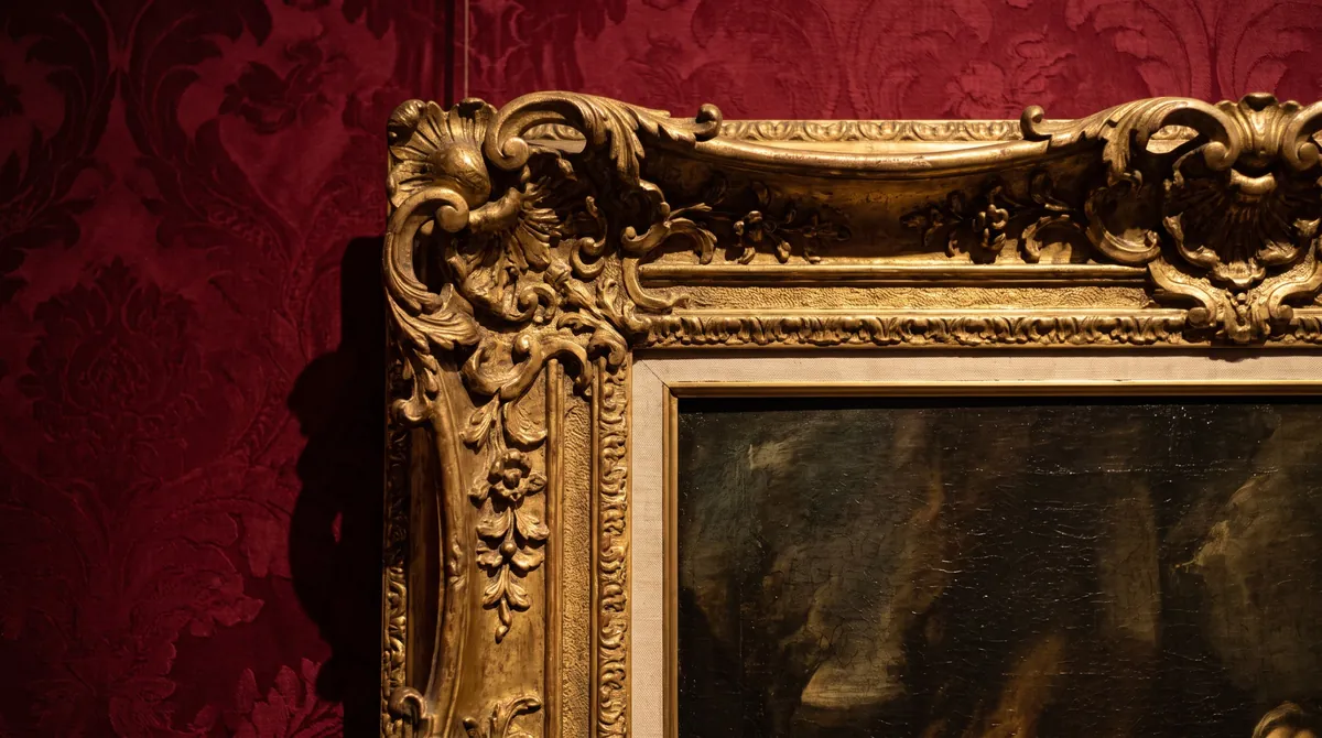 Corner of a carved gilded picture frame on a red damask wall