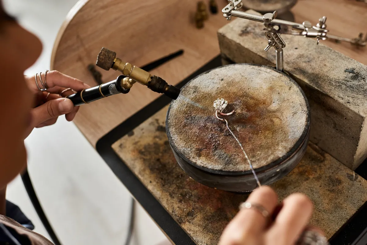 A goldsmith soldering a ring at a wooden jeweller’s bench