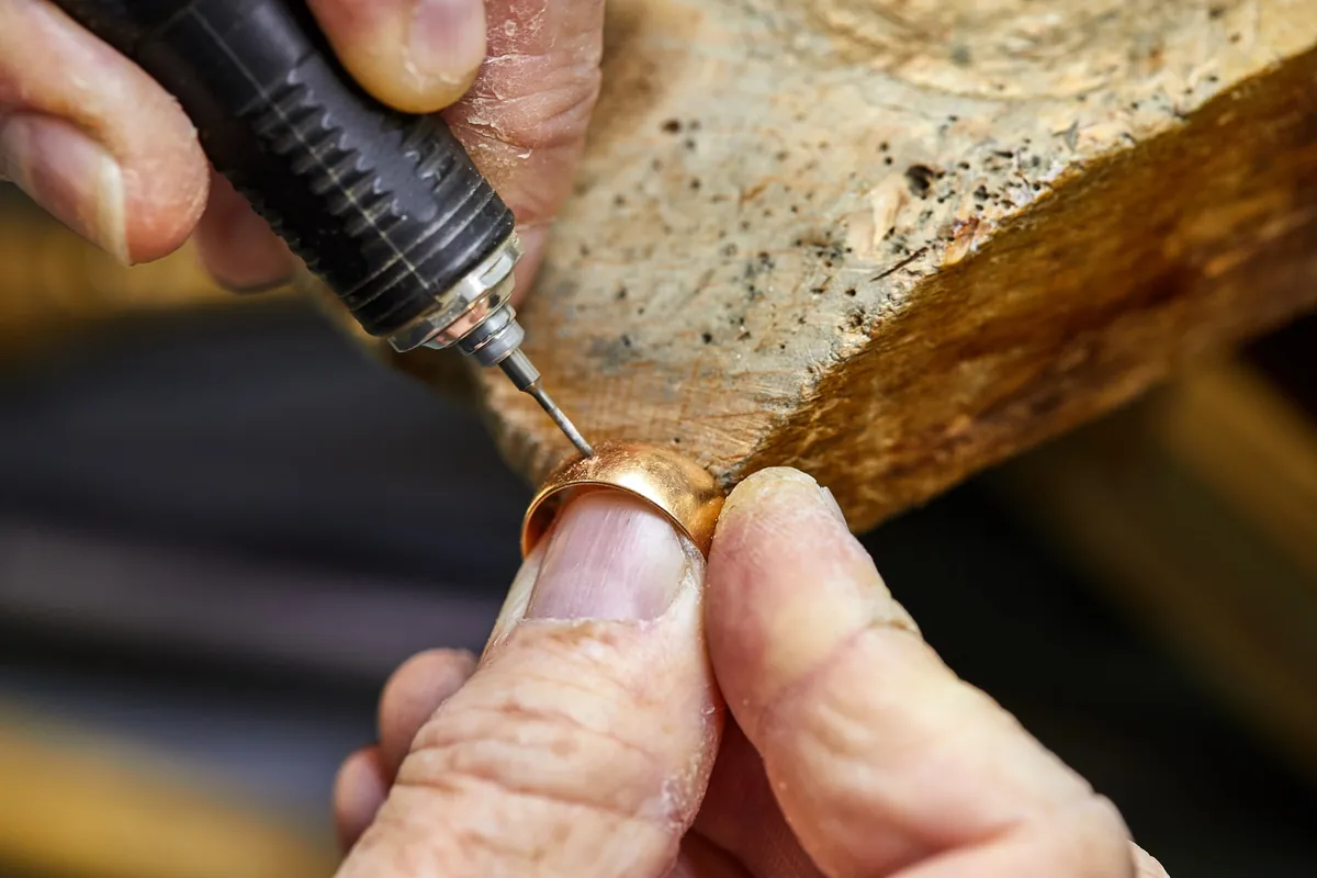 A goldsmith working on the inside of a gold ring with a fine tool